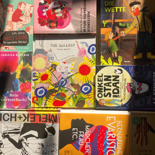 Das Kinderbuch Der Gagahof von Sabine Magnet liegt auf einem Büchertisch inmitten von anderen Büchern mit bunten Buchtiteln. Die Sonne scheint warm und gelblich auf die Bücher.