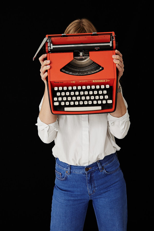 Das Foto zeigt die Verlagsgründerin und Autorin Sabine Magnet. Sie hält sich eine rote Schreibmaschine, eine Remington Riviera, vors Gesicht.
